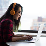 Teen student wearing headphones works on laptop.