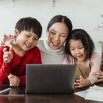 Mom and two small children smile at laptop screen.