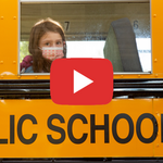 Masked student looks out of school bus window, with video play button overlay.